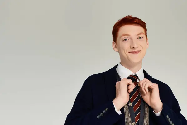 Un joven con el pelo rojo ajusta su corbata mientras muestra un traje de invierno de moda en un elegante estudio. - foto de stock