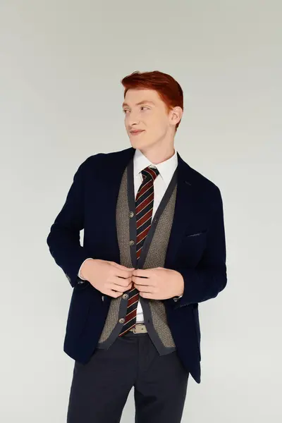 Un joven caballero con el pelo rojo vibrante muestra un sofisticado traje de invierno en capas en un estudio. - foto de stock