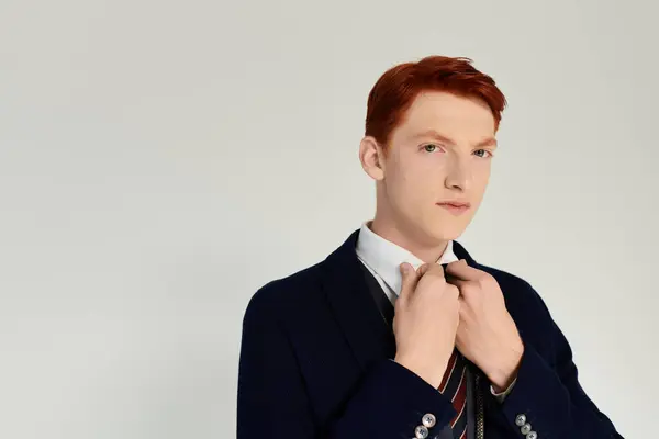 A young man in a layered winter outfit adjusts his tie, embodying sophistication and style in a modern studio. — Stock Photo