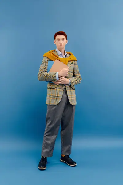 A young man with striking red hair stands confidently in a stylish winter outfit while holding a folder. — Stock Photo