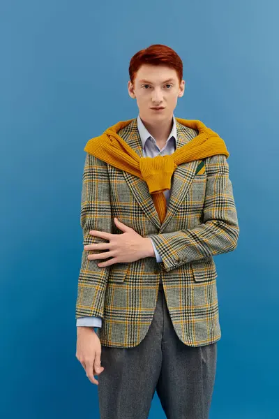 A man showcases a stylish winter outfit featuring layers and vibrant colors against a blue backdrop. — Stock Photo