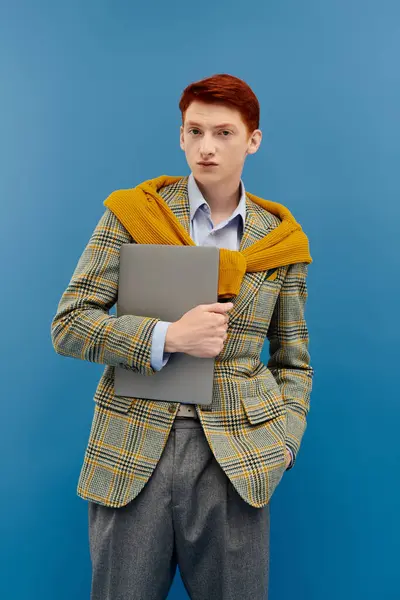 Un giovane alla moda mette in mostra un abito invernale stratificato, tenendo con fiducia un computer portatile in uno studio. — Foto stock