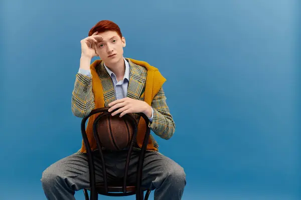 A young man with red hair poses confidently in layered winter attire while seated. — Stock Photo