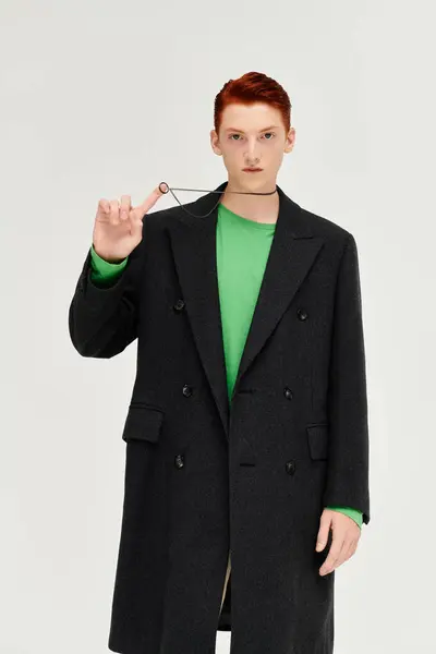 A young man with striking red hair models an elegant winter coat and vibrant top in a studio. — Stock Photo