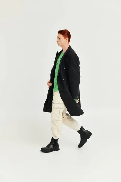 Un jeune homme aux cheveux roux saisissants met en valeur un manteau d'hiver à la mode tout en marchant dans un studio moderne. — Photo de stock