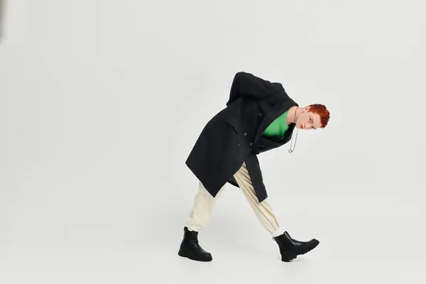 A young man with striking red hair showcases an elegant winter coat in a contemporary studio setting. — Stock Photo