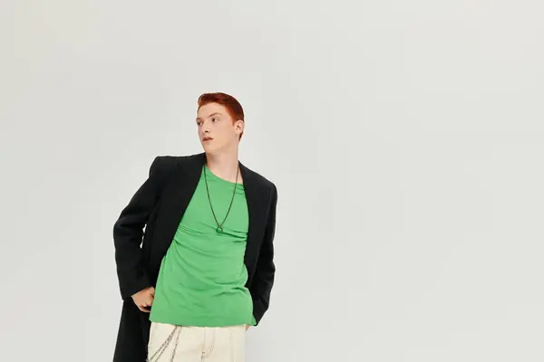 A young man with striking red hair showcases a fashionable winter coat while standing gracefully in a studio. — Stock Photo