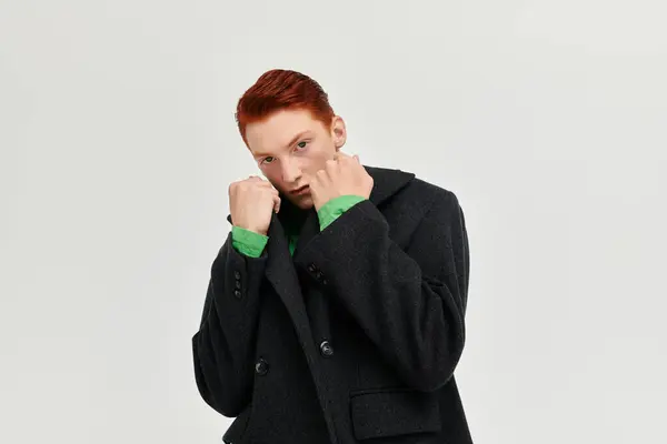 A stylish young man with red hair poses confidently in an elegant winter coat, exuding fashion flair. — Stock Photo