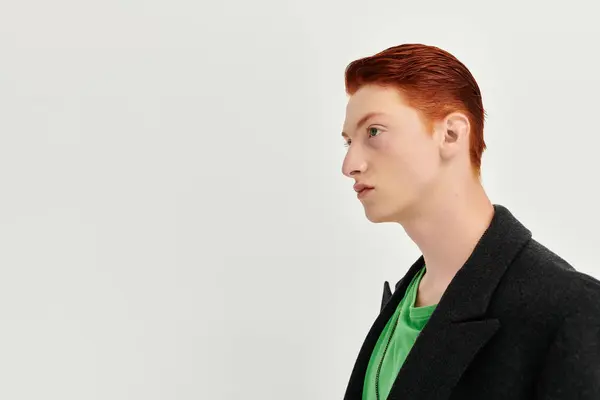 Un giovane uomo con i capelli rossi vibranti mette in mostra il suo cappotto invernale alla moda in un ambiente moderno monolocale. — Foto stock