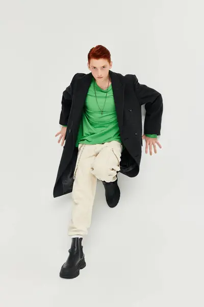 A fashionable man with striking red hair showcases a chic winter coat and lively attitude in studio light. — Stock Photo