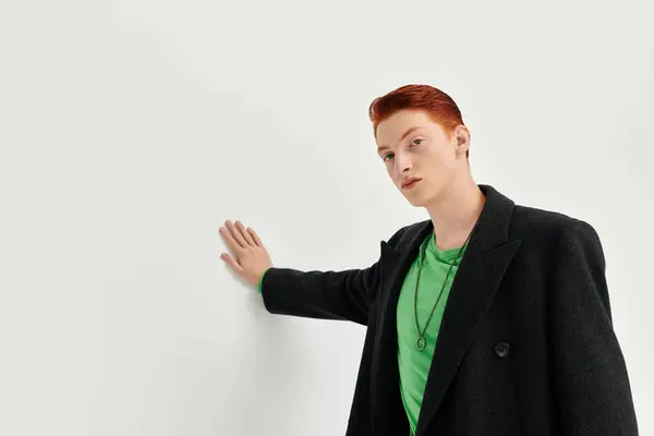 A fashionable young man with striking red hair showcases an elegant coat and a casual shirt in a studio. — Stock Photo