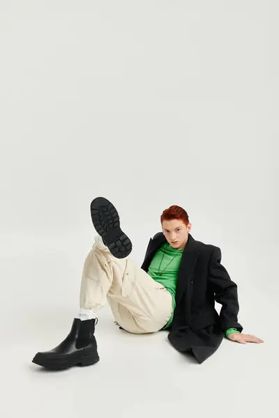 A young man with vibrant red hair poses in an elegant winter coat, exuding confidence in a chic studio. — Stock Photo