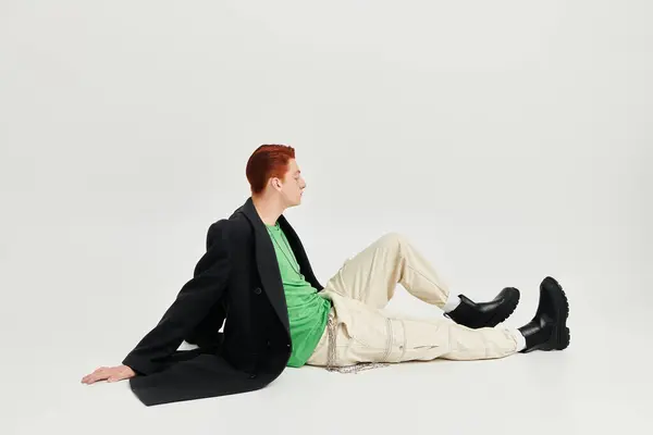 A fashionable young man with striking red hair sits confidently in a studio, showcasing his winter coat. — Stock Photo