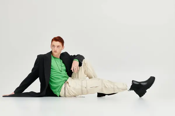 A young, handsome man with striking red hair showcases bold fashion choices in a studio environment. — Stock Photo
