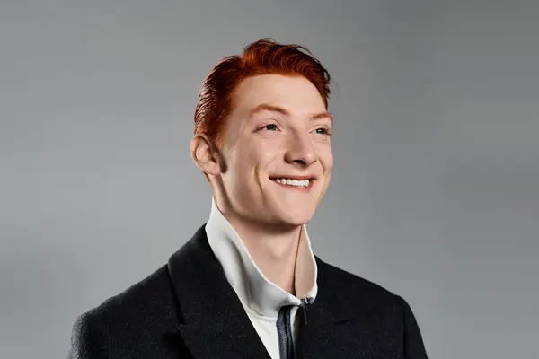 A confident young man with vibrant red hair smiles warmly while dressed in a fashionable winter coat. — Stock Photo