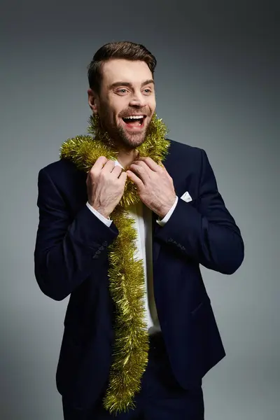A cheerful young man wearing a suit playfully showcases holiday spirit with shiny decorations. — Stock Photo