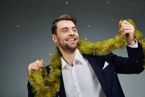 A handsome young man wears a festive outfit, joyfully holding decorative tinsel while smiling. — Stock Photo