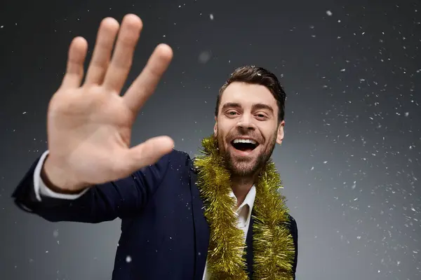 A handsome young man with a big smile waves while adorned in a festive holiday garland. — Stock Photo