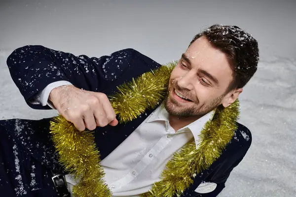 A joyful young man wearing a suit is playfully surrounded by snow and festive tinsel. — Stock Photo