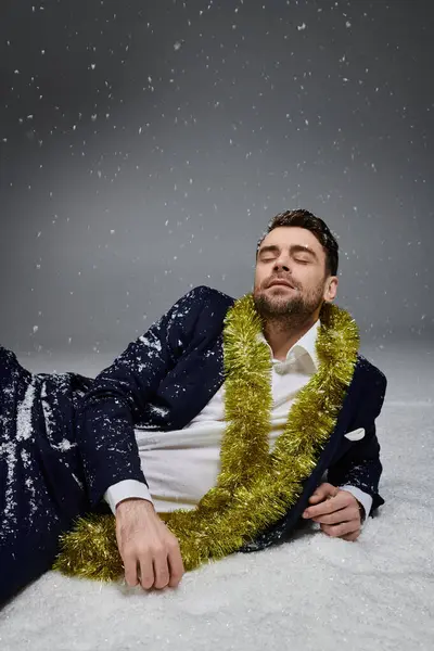 A stylish young man lounges gracefully amidst falling snowflakes, adorned with festive greenery. — Stock Photo