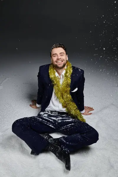 Cheerful young man relaxes in snowy surroundings wearing a stylish suit and festive decorations. — Stock Photo