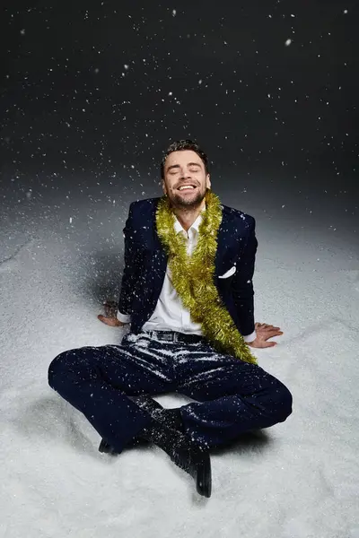 Un giovane uomo è seduto nella neve soffice con un sorriso allegro, decorato con decorazioni festive. — Foto stock
