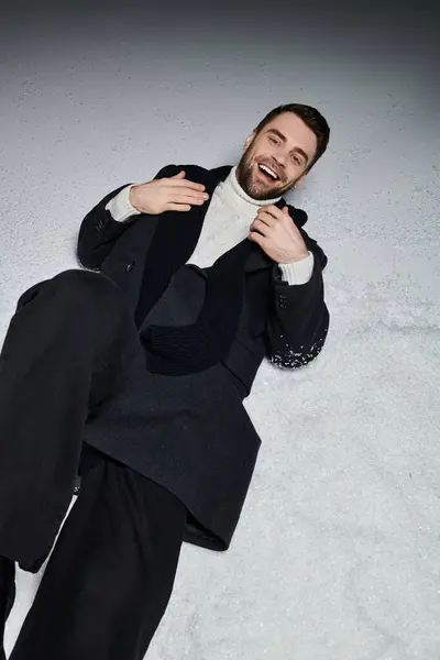 A young man laughing joyfully while lying in the snow, surrounded by a winter landscape. — Stock Photo