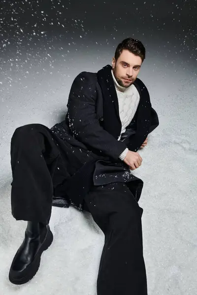 Um jovem reclina-se no chão coberto de neve, vestido calorosamente enquanto flocos de neve caem ao seu redor. — Fotografia de Stock