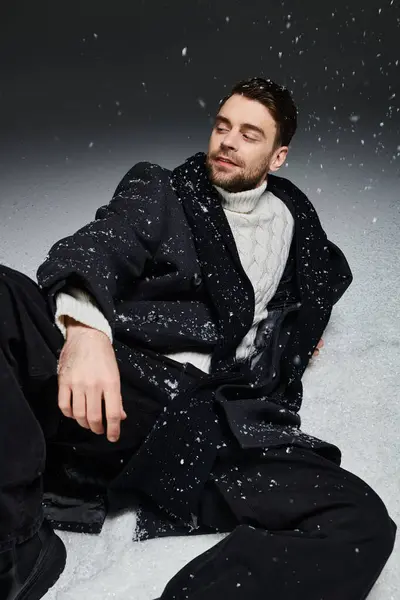 A beautiful winter day with a young man enjoying snowflakes while seated in a cozy outfit. — Stock Photo