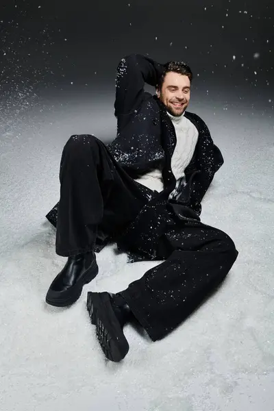 The handsome young man relaxes in the snow, sporting trendy winter clothing and smiling brightly. — Stock Photo