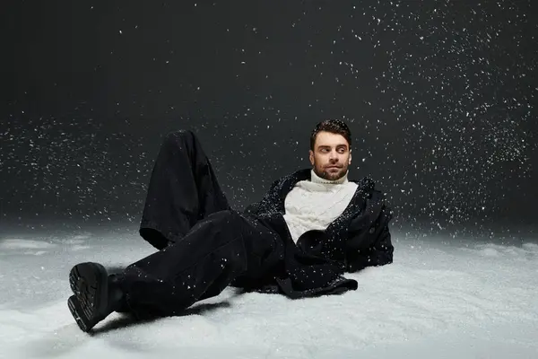 A handsome young man lounges peacefully in a snowy setting, showcasing modern winter attire. — Foto stock