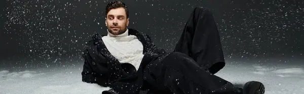 Un giovane elegante si rilassa giocosamente nella neve, guardando bello in abbigliamento invernale. — Foto stock