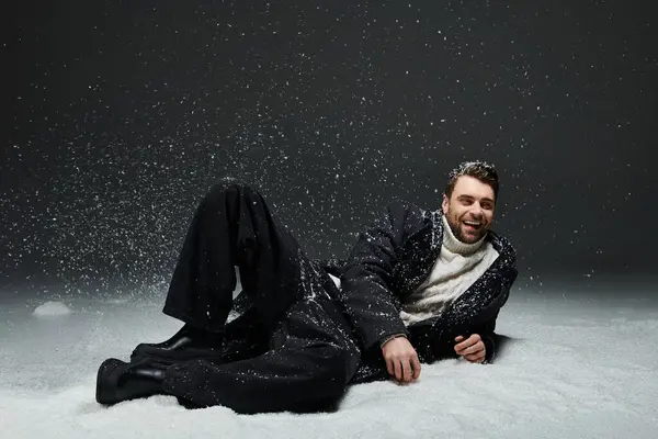 Un joven alegre yace en la nieve, abrazando el frío invernal y sonriendo brillantemente. - foto de stock