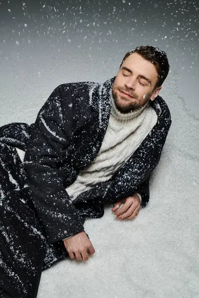 A handsome young man relaxes in soft, falling snow, embracing the winter seasons beauty. — Stock Photo