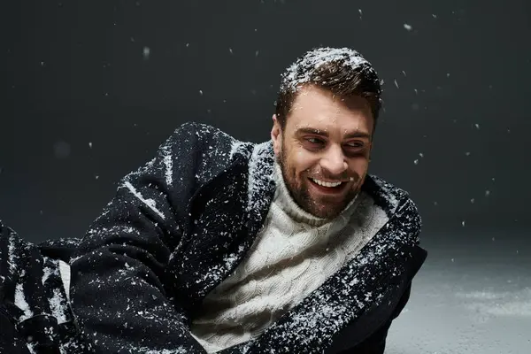 A cheerful young man enjoying a playful moment while surrounded by falling snow indoors. — Stock Photo