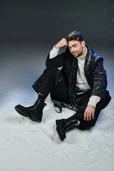 A young man with a charming expression relaxes in the snow, dressed in winter fashion. — Stock Photo