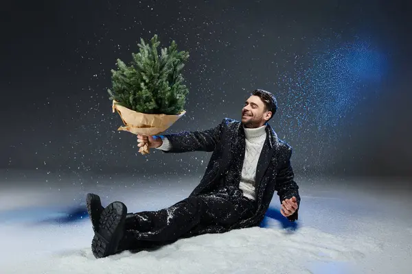 Un giovane vestito con abiti eleganti gode della stagione invernale mentre tiene in mano un albero. — Foto stock