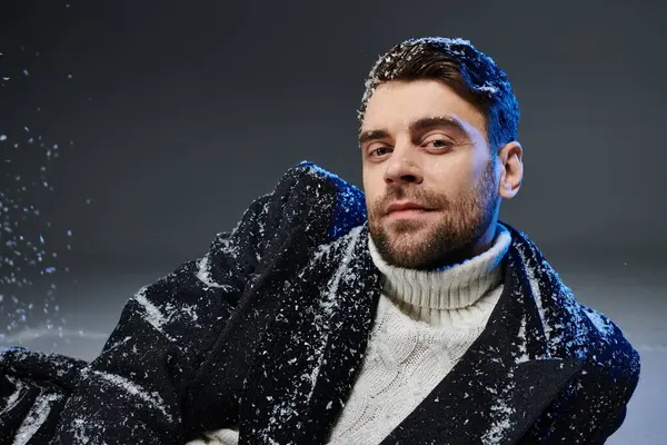 Un joven confiado se relaja en un fondo nevado, exudando encanto y calidez en atuendo de invierno - foto de stock
