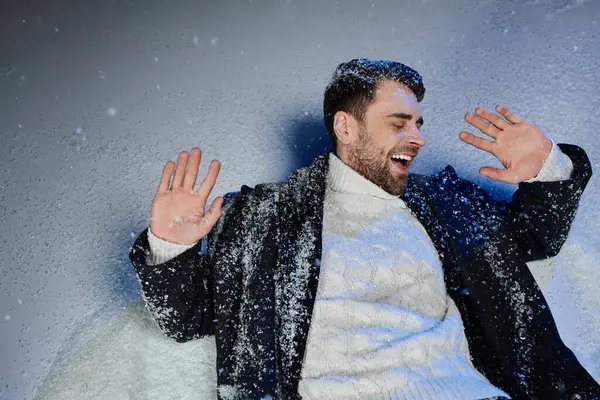 A handsome young man laughs while enjoying a playful moment in fresh snowflakes. — Stock Photo