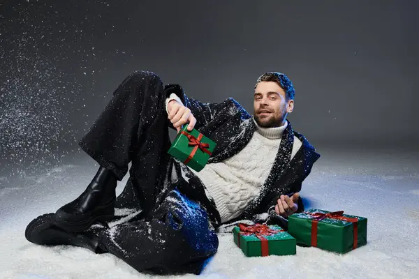 A handsome young man relaxes in a snowy backdrop, playfully holding wrapped holiday presents. — Stock Photo