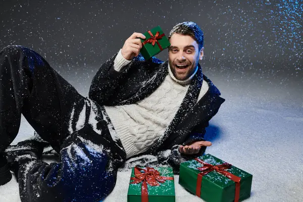 A cheerful young man surrounded by snow joyfully holds a gift while sitting beside others. — Photo de stock