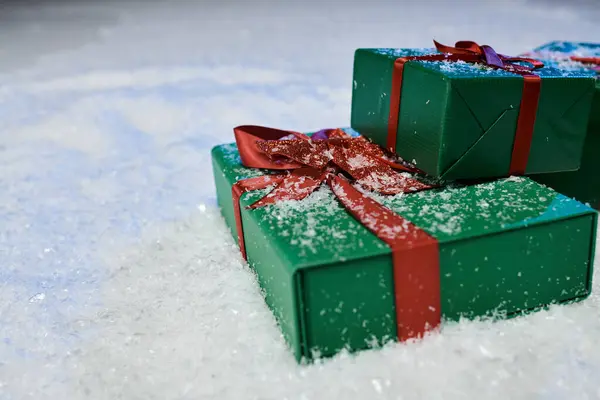 Due splendidamente avvolti regali verdi con nastri rossi siedono tranquillamente su una coperta di neve scintillante. — Foto stock