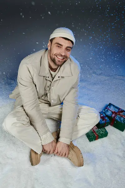 A cheerful young man sits in a snowy setting, radiating warmth and holiday spirit. — Stock Photo