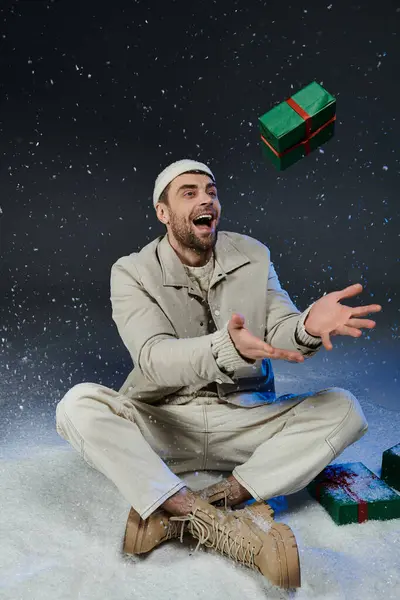 A cheerful young man laughs and playfully throws a wrapped present in a snowy winter setting. — Stock Photo
