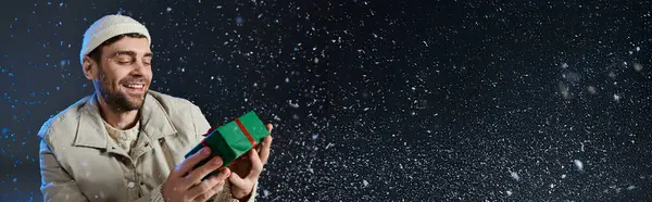 A young man smiles brightly as he opens a colorful present, enjoying the snowy atmosphere. — Stock Photo