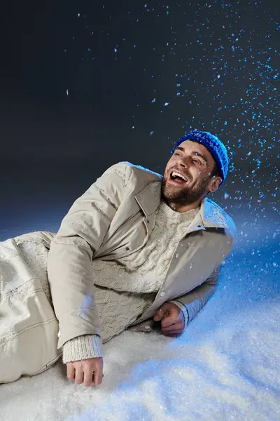 A young man dressed warmly smiles brightly as snowflakes dance around him in winter. — Stock Photo
