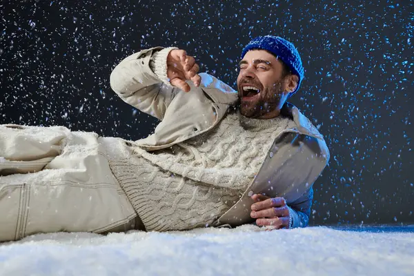 A young man laughs while lying in the snow, embracing the joy of winter in a playful atmosphere. — Stock Photo