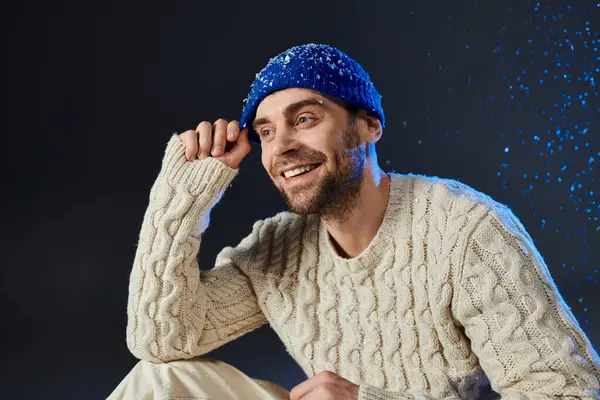 A joyful young man seated in a cozy sweater and hat, radiating warmth and happiness — Stock Photo