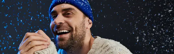 A cheerful young man embraces the winter season, smiling amidst falling snowflakes. — Stock Photo