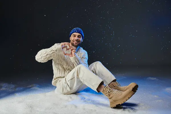 Un giovane allegro in un maglione accogliente e stivali gioca nella neve fresca sotto le luci della sera. — Foto stock
